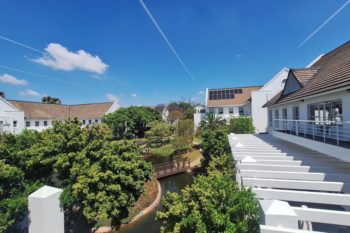 An elevated view of the office complex exterior, featuring well-maintained buildings with solar panels, a pergola, and a landscaped garden with a water feature.