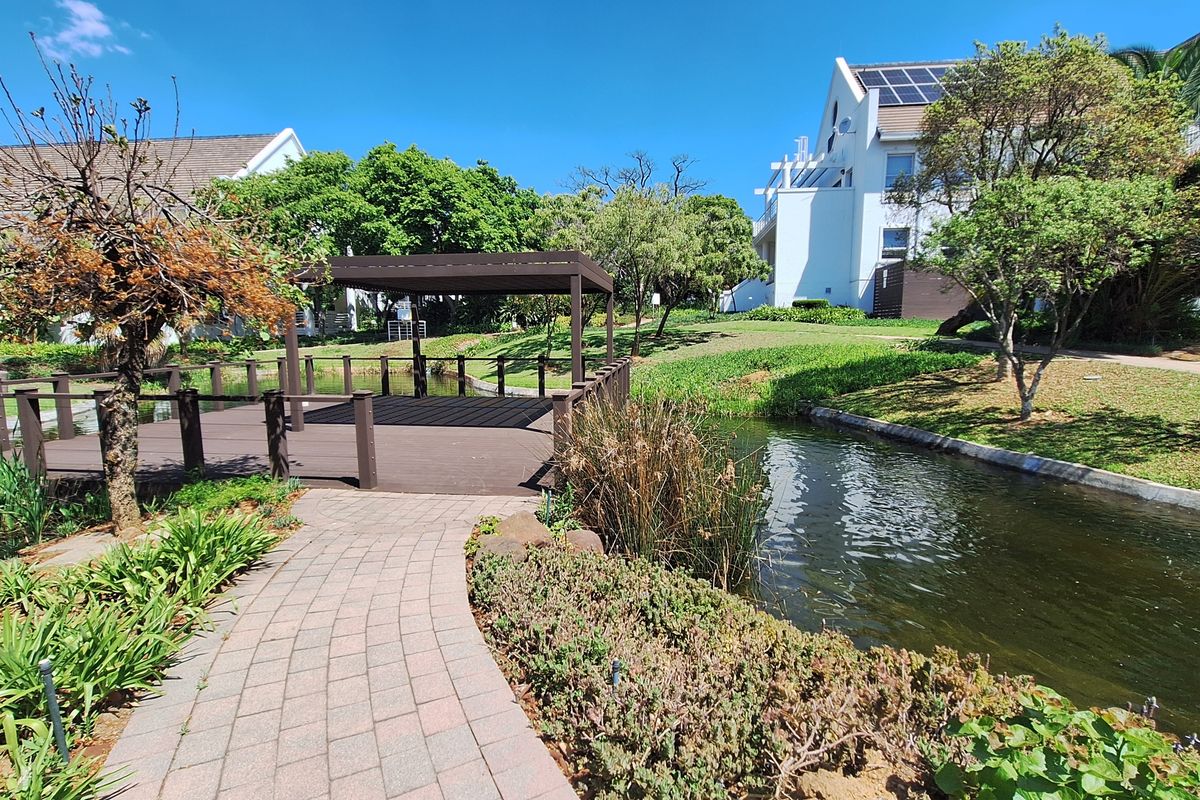 A well-maintained garden area featuring a timber deck with a pergola, a paved walkway, and a scenic water feature within the office complex grounds.
