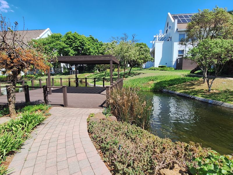 A well-maintained garden area featuring a timber deck with a pergola, a paved walkway, and a scenic water feature within the office complex grounds.