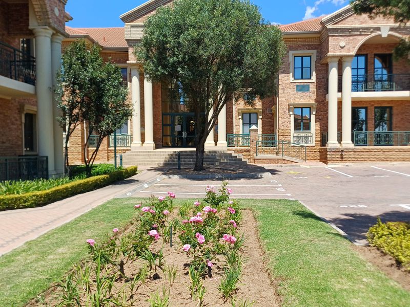 A well-maintained office building facade featuring classical architectural elements, brick construction, paved parking area, and landscaped garden frontage.