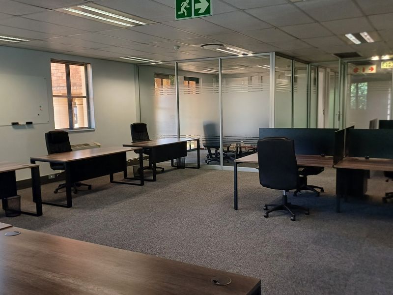 A professional open-plan office space featuring glass partitions, suspended ceilings with recessed lighting, and carpeted flooring.