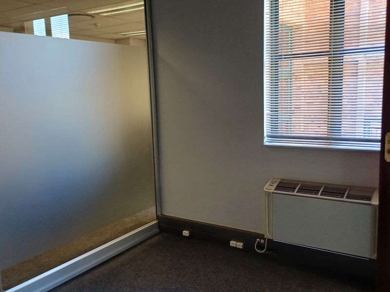 A vacant office space featuring a frosted glass partition, carpeted flooring, venetian blinds, and a built-in HVAC unit.