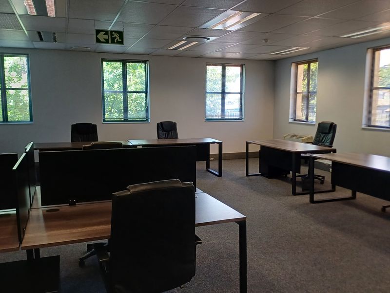 A spacious, well-lit office area featuring suspended ceilings, recessed lighting, and large windows with venetian blinds, providing a professional and functional workspace environment.
