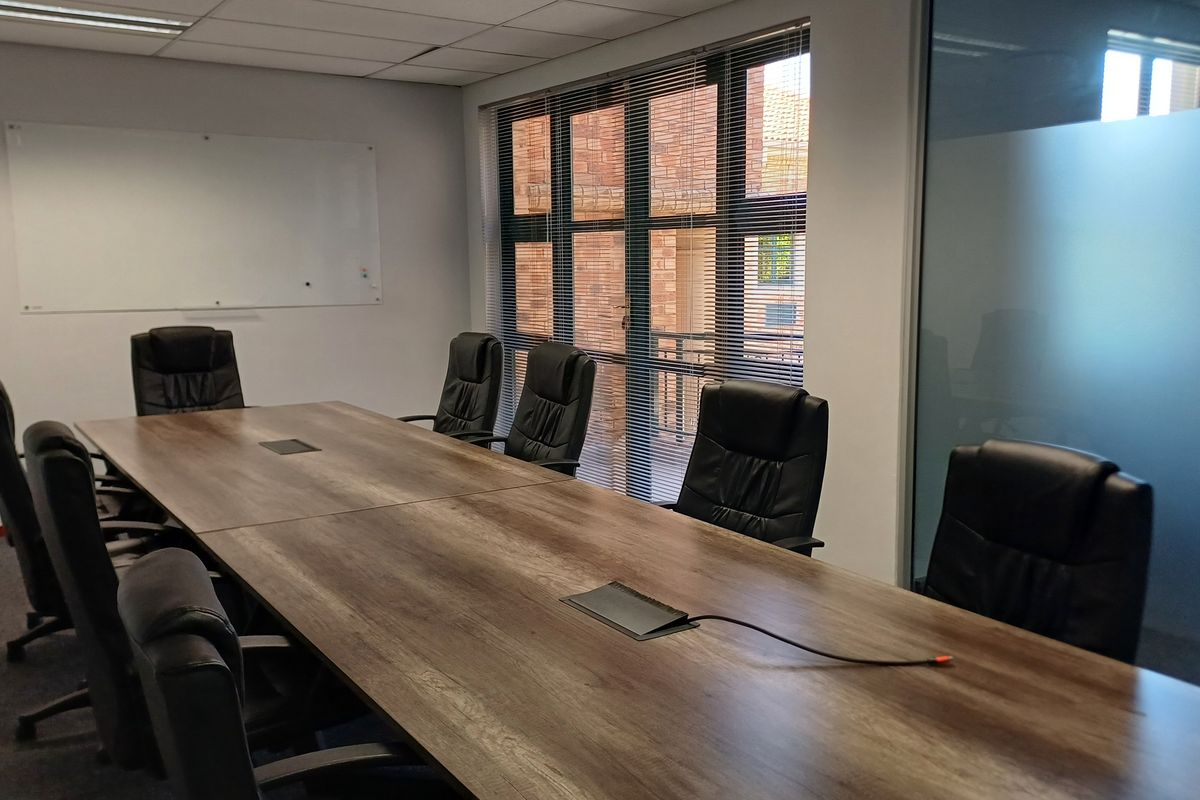 A professional boardroom featuring a large meeting table, wall-mounted whiteboard, frosted glass partition, and ample natural light through large windows.