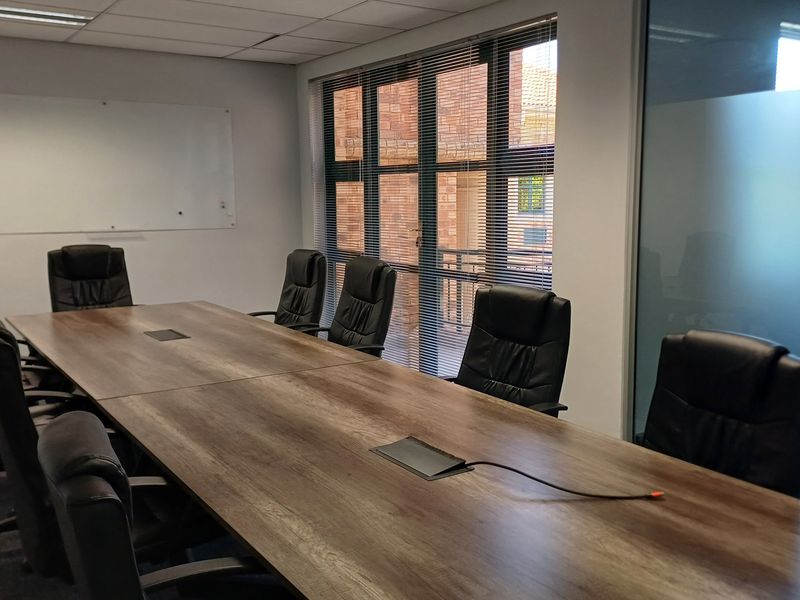 A professional boardroom featuring a large meeting table, wall-mounted whiteboard, frosted glass partition, and ample natural light through large windows.