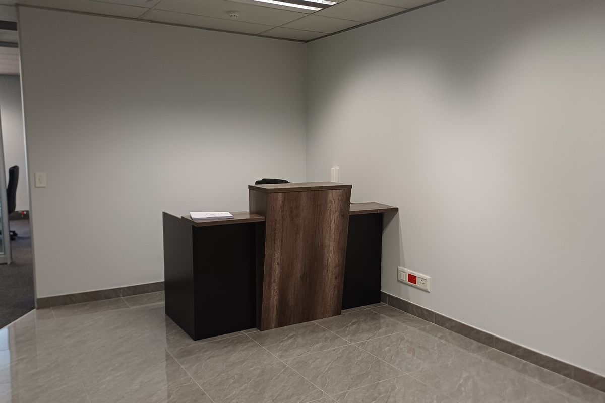 A professional office reception area featuring a modern wood-finish desk, polished tiled flooring, and clean neutral walls.