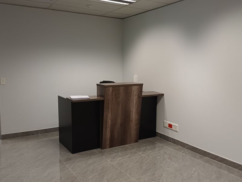 A professional office reception area featuring a modern wood-finish desk, polished tiled flooring, and clean neutral walls.