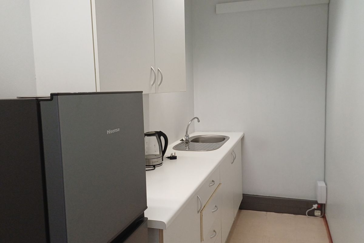 A compact office kitchenette featuring white built-in cabinetry, a laminate countertop, and a stainless steel sink.