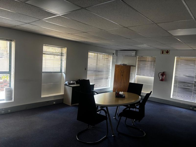 A functional office space featuring a suspended ceiling, air conditioning, multiple windows with venetian blinds, and carpeted flooring.