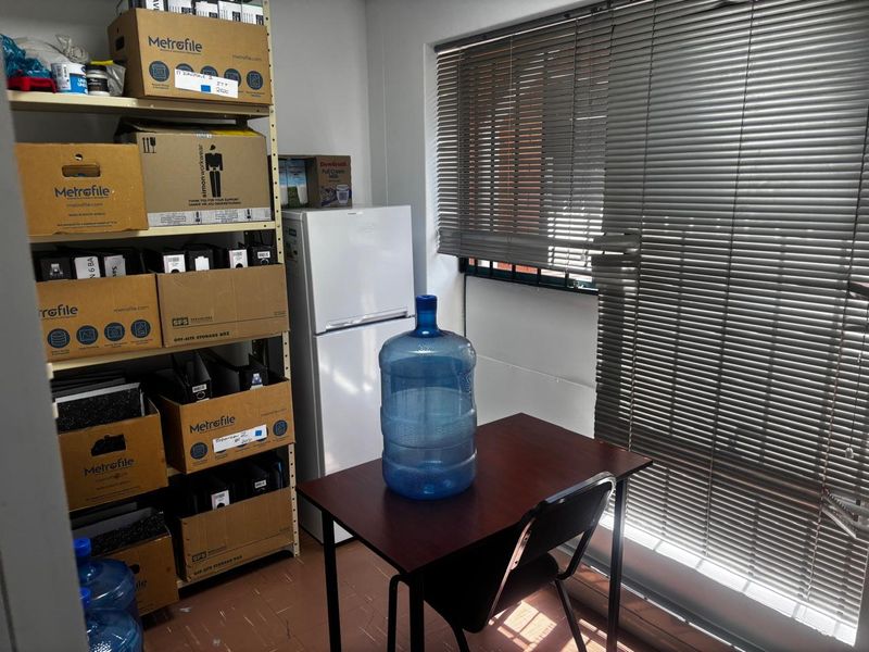 A functional utility or storage space featuring tiled flooring and venetian blinds, currently utilized for document storage and basic office amenities.