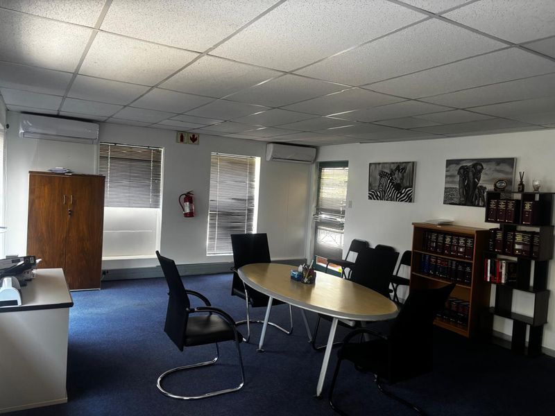 A functional office space featuring a suspended ceiling, dual split-system air conditioning units, carpeted flooring, and venetian blinds for light control.
