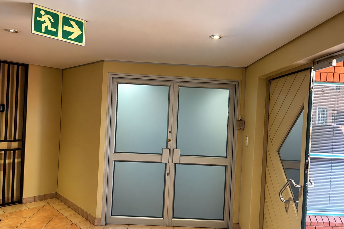 A clean and functional office entry area featuring frosted glass double doors, tiled flooring, and integrated emergency exit signage.