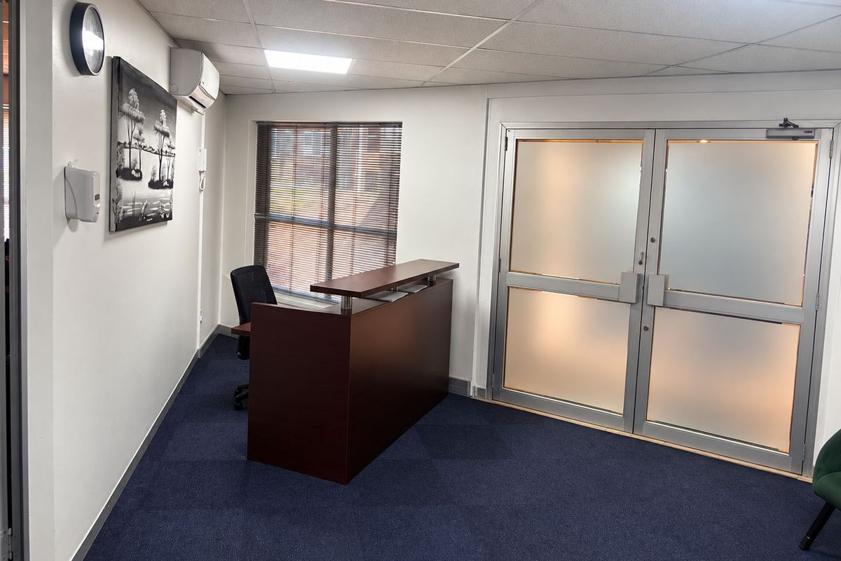A professional office space featuring carpeted flooring, a suspended ceiling, air conditioning, and frosted glass double doors providing a bright and functional work environment.