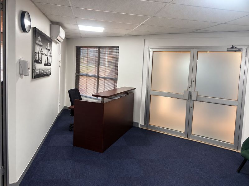 A professional office space featuring carpeted flooring, a suspended ceiling, air conditioning, and frosted glass double doors providing a bright and functional work environment.
