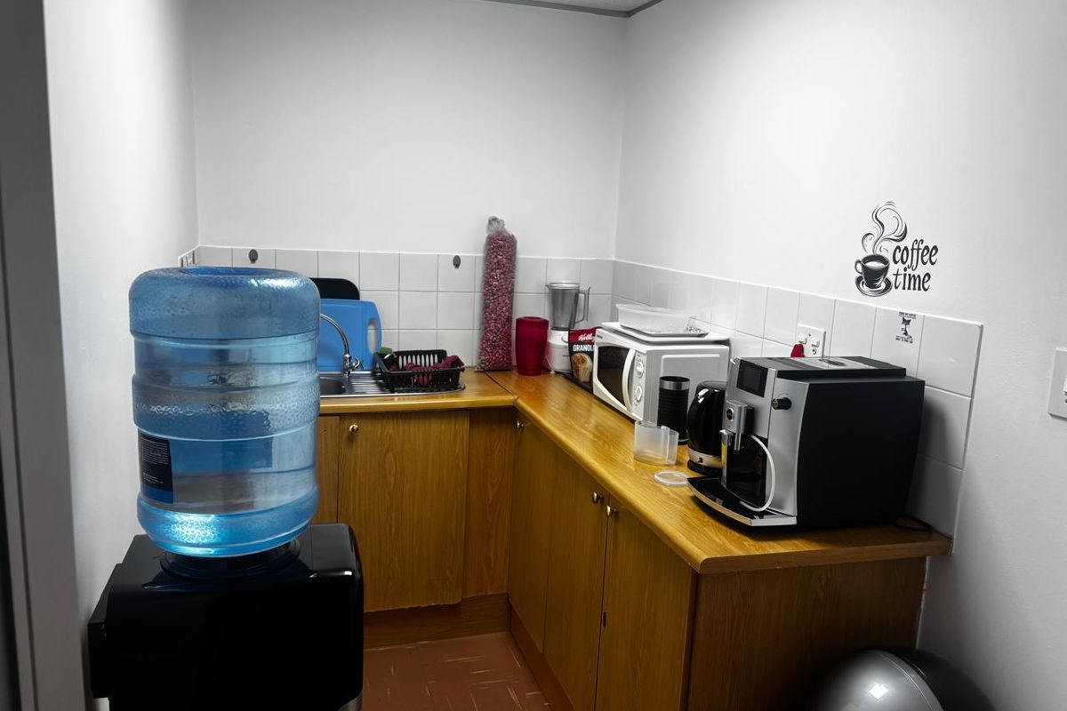 A compact office kitchenette featuring laminate cabinetry, a stainless steel sink, and tiled backsplash, providing a functional space for staff refreshments.