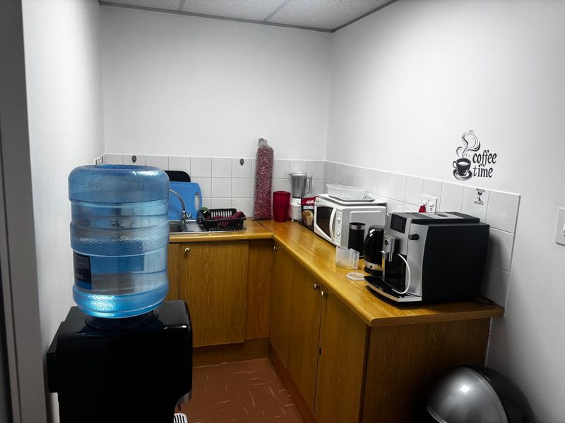 A compact office kitchenette featuring laminate cabinetry, a stainless steel sink, and tiled backsplash, providing a functional space for staff refreshments.