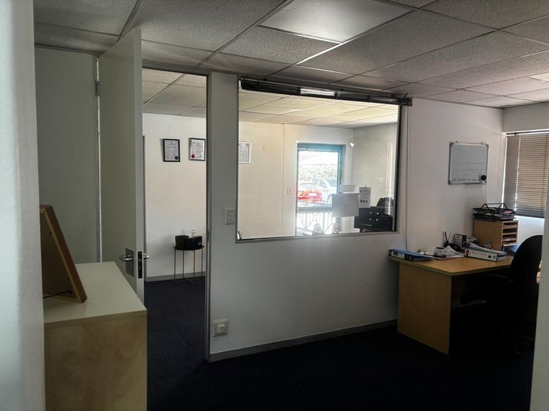 A functional office space featuring a glass partition, suspended ceiling, and carpet flooring, providing a professional environment with natural light.