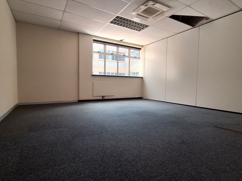 An empty office space featuring carpeted flooring, partition walls, and a suspended ceiling with recessed lighting and a missing tile.
