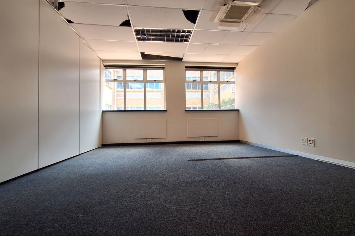 An empty office space featuring carpet flooring, built-in wall panels, and a suspended ceiling in need of repair.