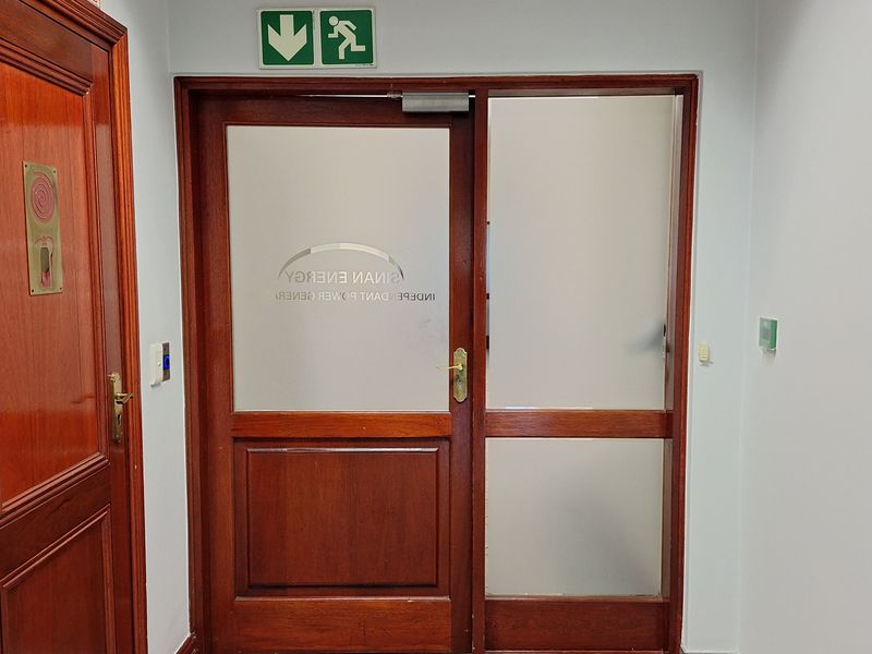 A professional office entrance featuring a wooden door with frosted glass panels, tiled flooring, and clear fire safety signage.