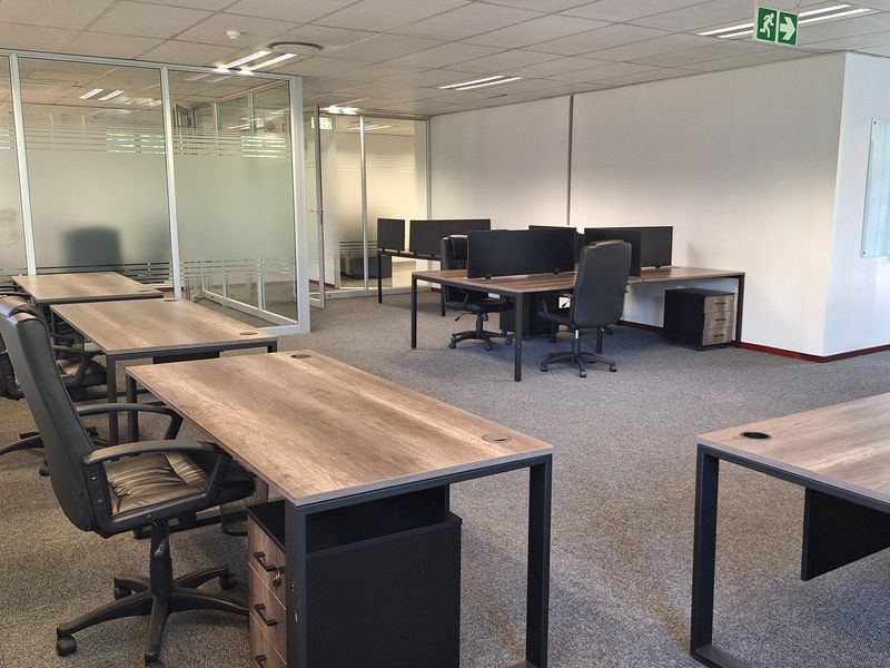 Modern open-plan office space featuring glass partitioning, suspended ceilings with recessed lighting, and carpeted flooring.