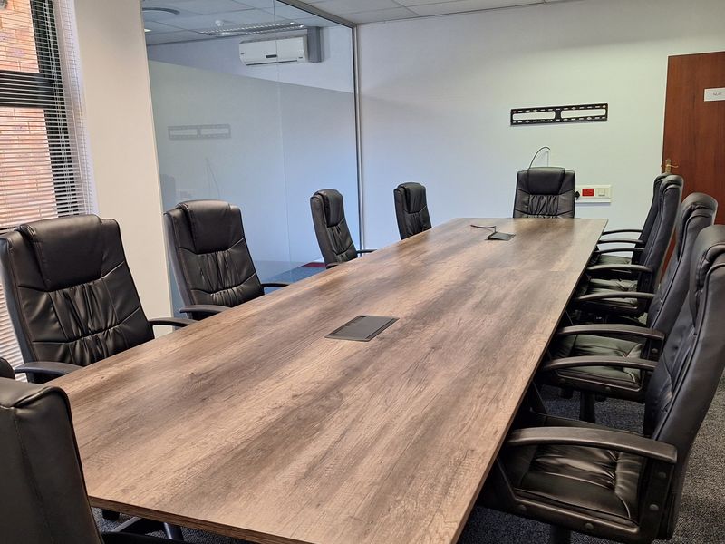A professional boardroom featuring a large meeting table, glass partition wall, suspended ceiling with recessed lighting, and carpeted flooring.