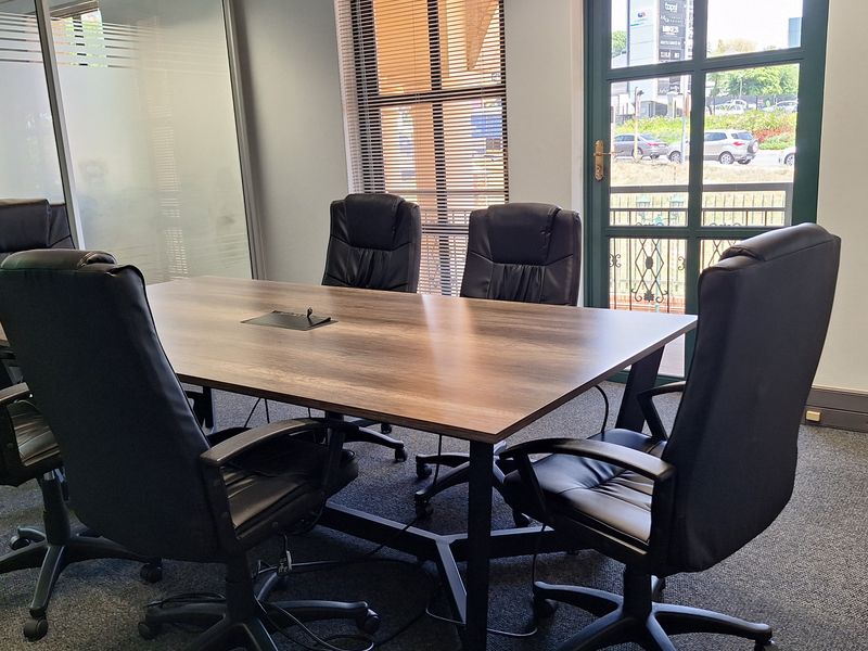 A professional office meeting room featuring carpet flooring, a glass partition, and a glass door with natural light and venetian blinds.