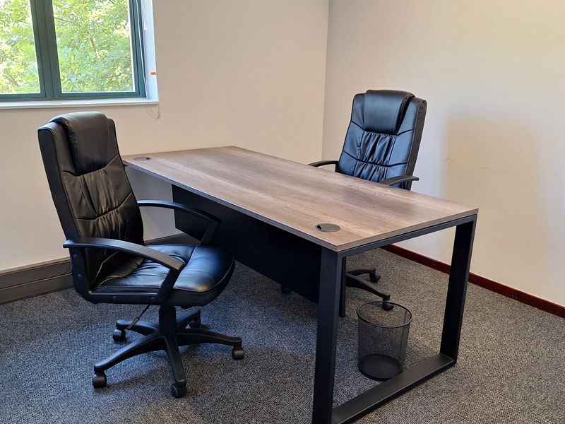 A functional office space featuring carpeted flooring and a window with venetian blinds, providing a clean and professional work environment.