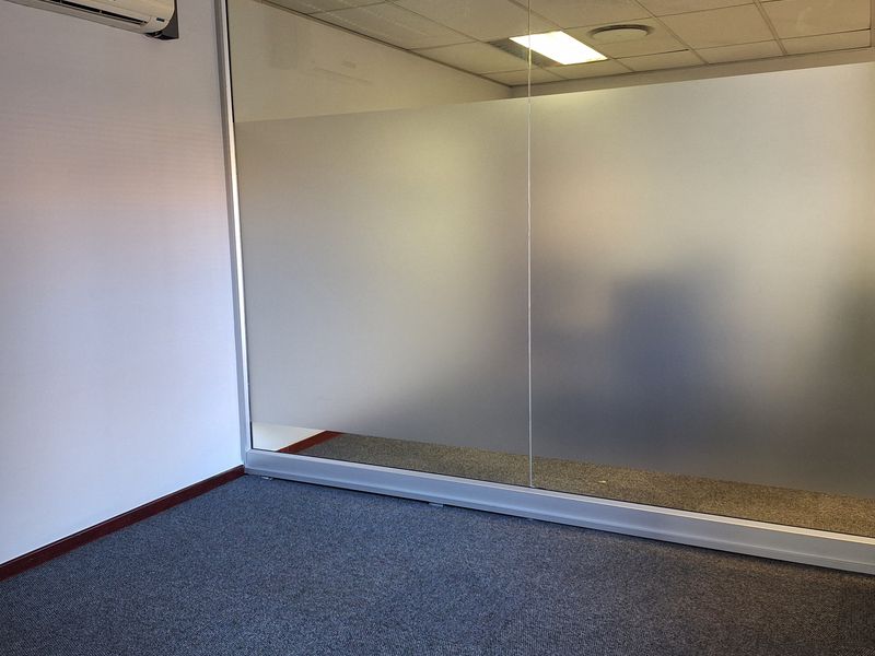 A clean, empty office space featuring a modern frosted glass partition, suspended ceiling with recessed lighting, and wall-mounted air conditioning.