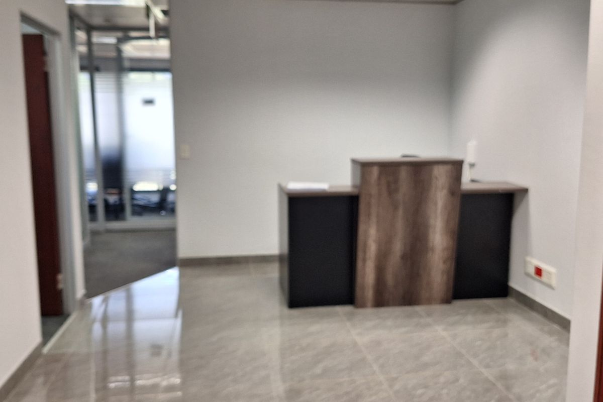 A professional office entry area featuring polished tiled flooring, a built-in reception desk, and a suspended ceiling with integrated lighting.