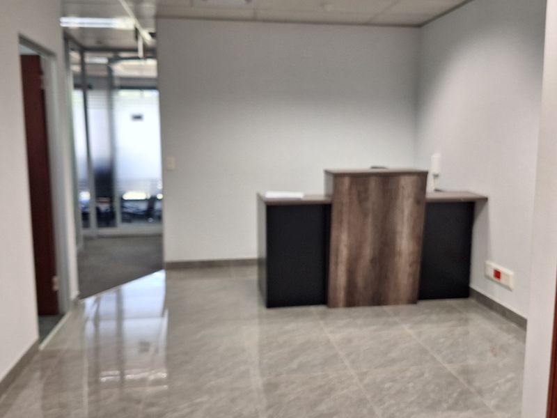 A professional office entry area featuring polished tiled flooring, a built-in reception desk, and a suspended ceiling with integrated lighting.
