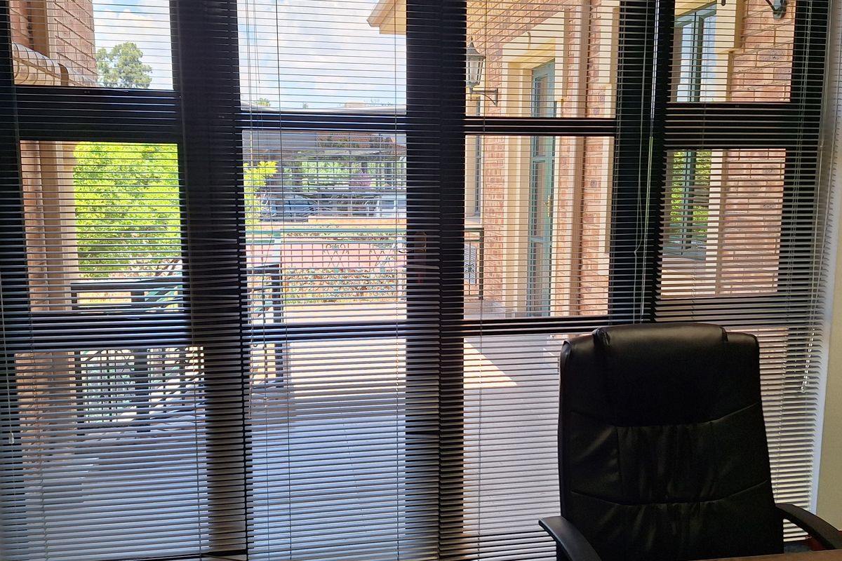 A professional office space featuring large windows with venetian blinds, providing natural light and views of the exterior building facade.