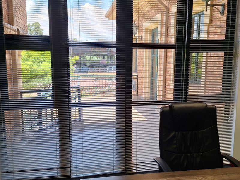 A professional office space featuring large windows with venetian blinds, providing natural light and views of the exterior building facade.