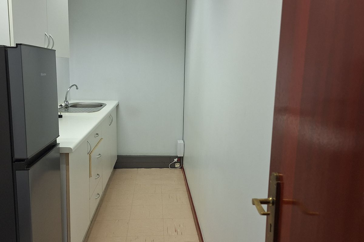 A compact office kitchenette featuring white built-in cabinetry, a stainless steel sink, and durable vinyl flooring.