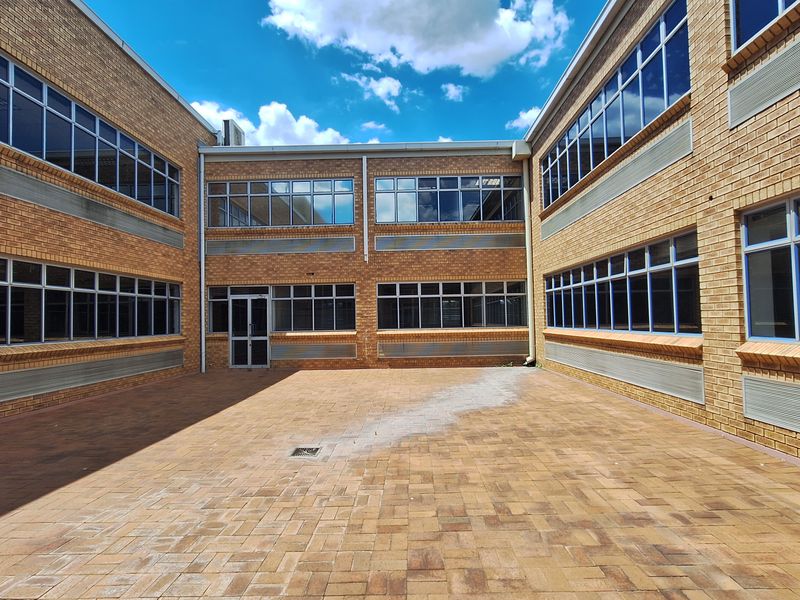 A spacious paved courtyard area enclosed by a multi-story brick office building with extensive aluminium-framed windows.