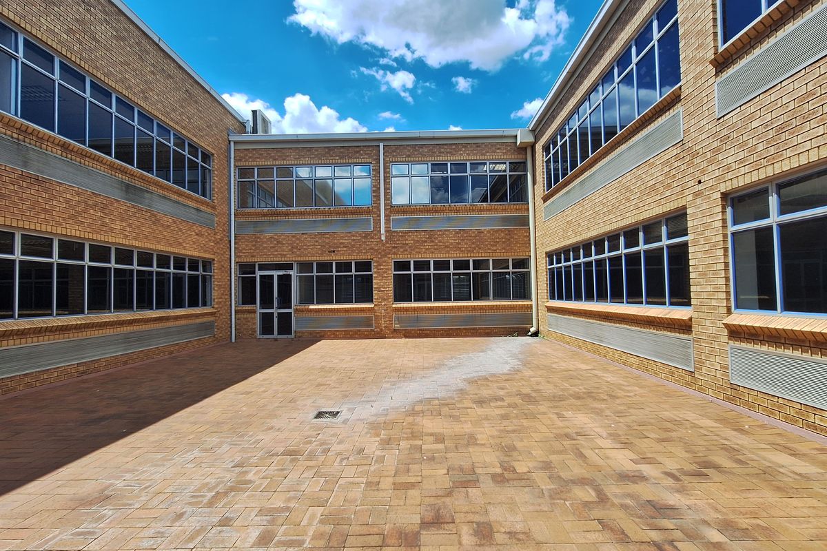 A spacious paved courtyard area enclosed by a multi-story brick office building with extensive aluminium-framed windows.