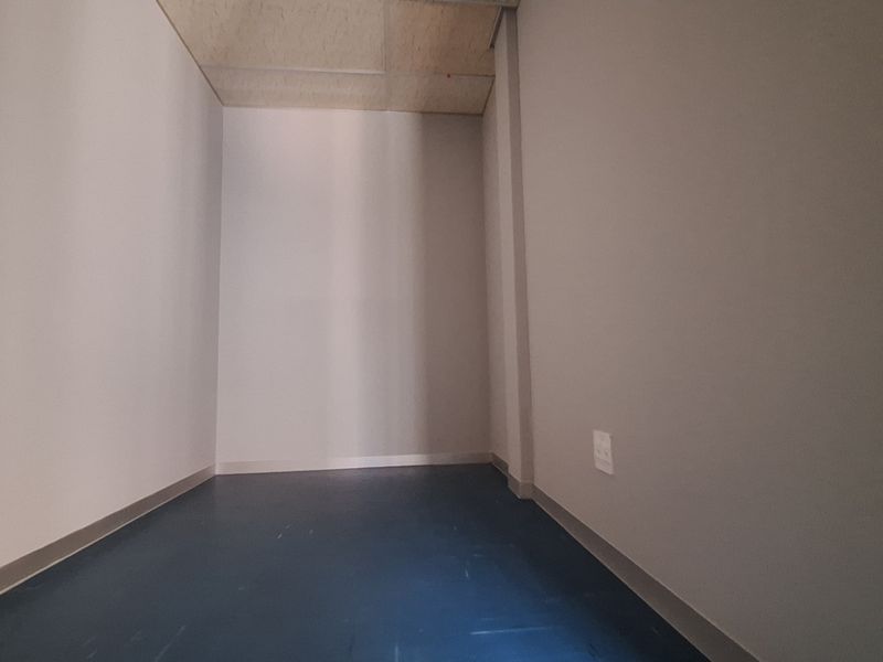 A clean, empty office space featuring neutral walls, durable vinyl flooring, and a suspended ceiling, suitable for a professional workspace.
