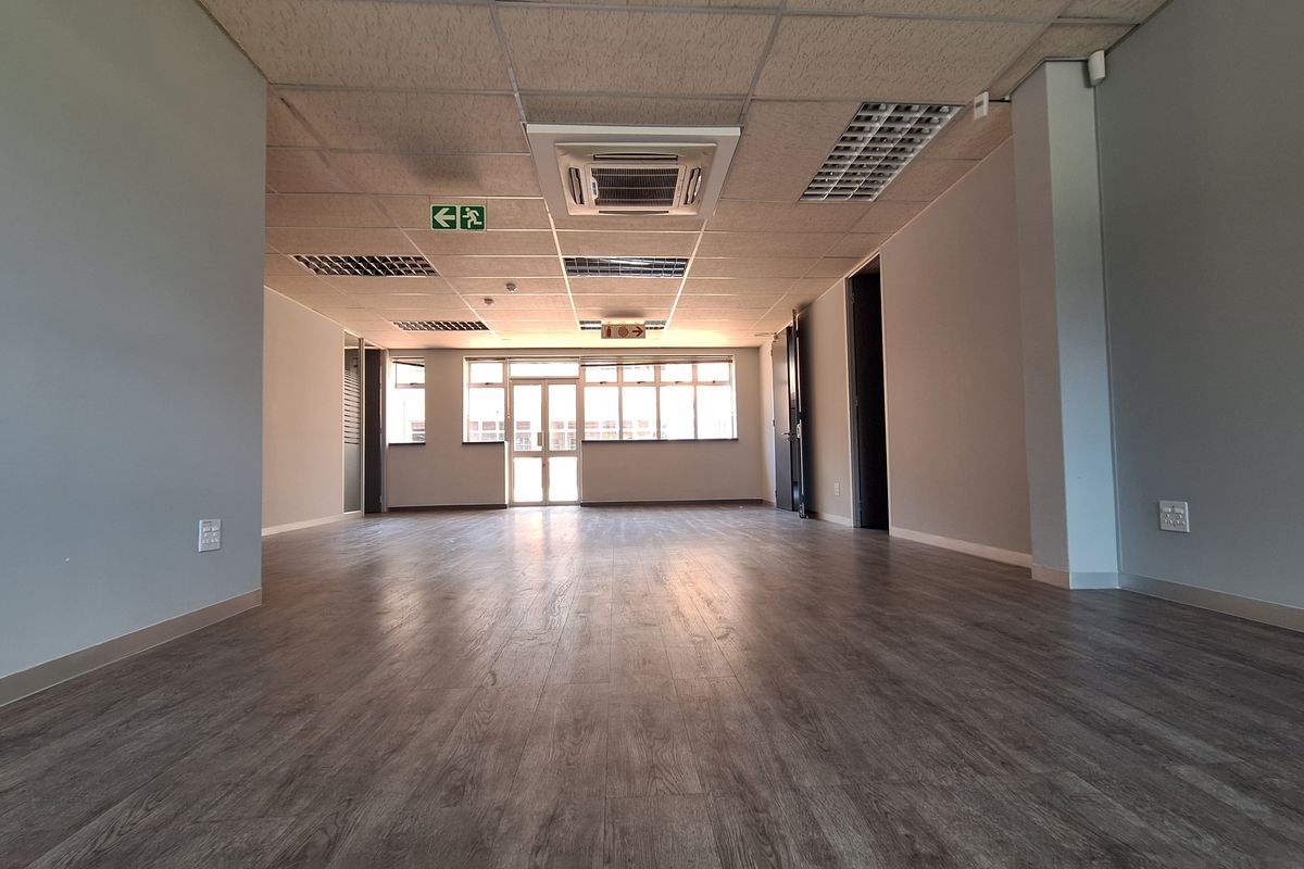 A spacious, vacant office area featuring modern laminate flooring, a suspended ceiling with integrated lighting, and a cassette air conditioning unit.