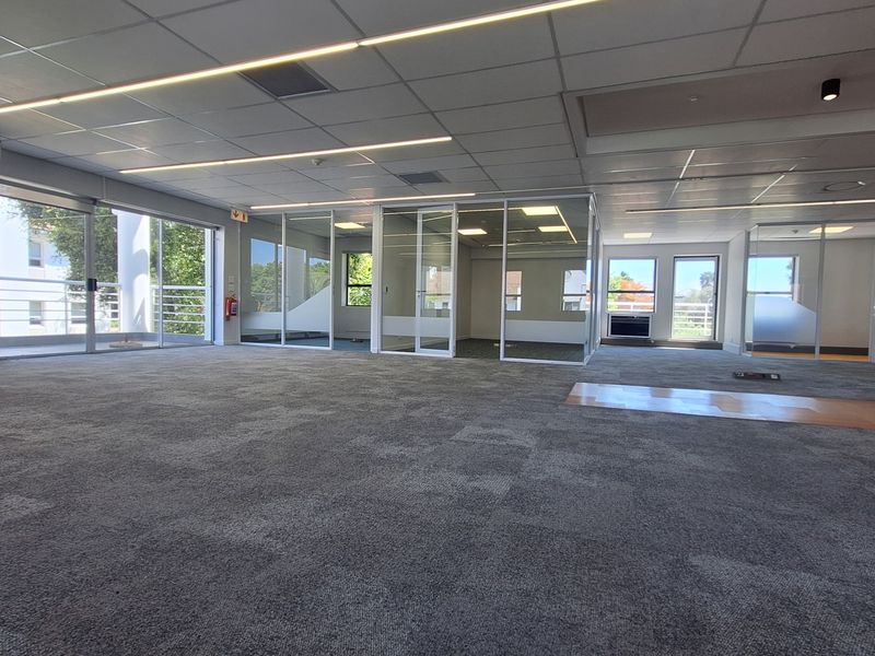 Spacious open-plan office area featuring modern glass partitions, suspended ceilings with integrated lighting, and durable carpet tile flooring.