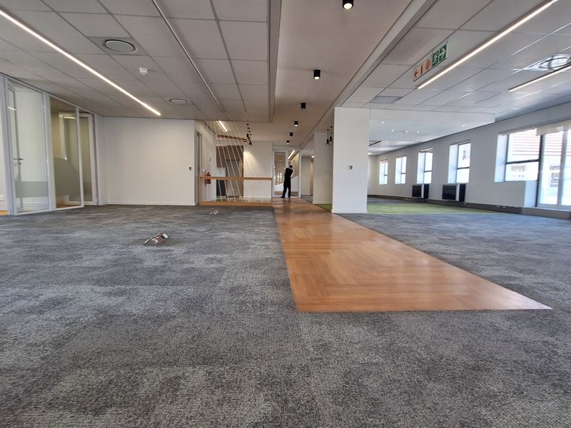 Spacious open-plan office area featuring a mix of carpet and parquet flooring, modern recessed lighting, and glass-partitioned private offices.