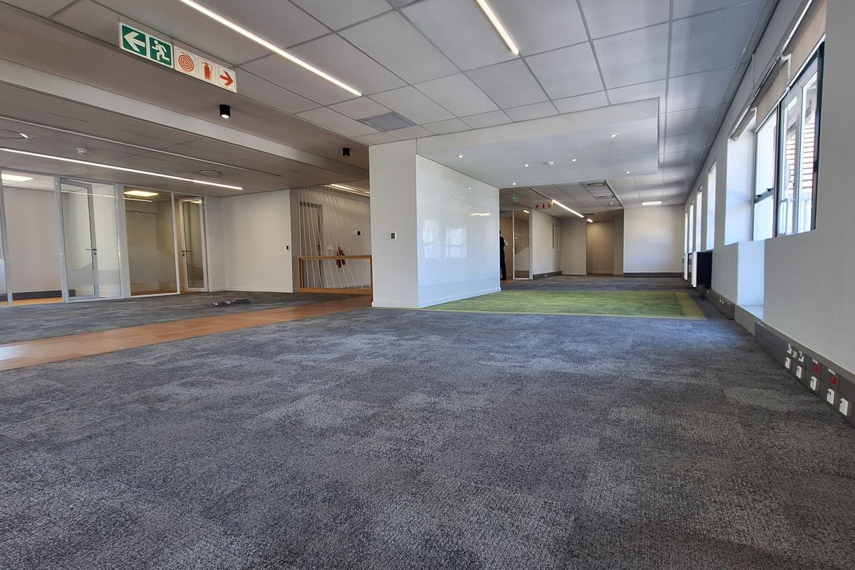 Spacious open-plan office area featuring modern carpet tiles, suspended ceilings with recessed lighting, and glass-partitioned meeting rooms, offering a clean and professional workspace.