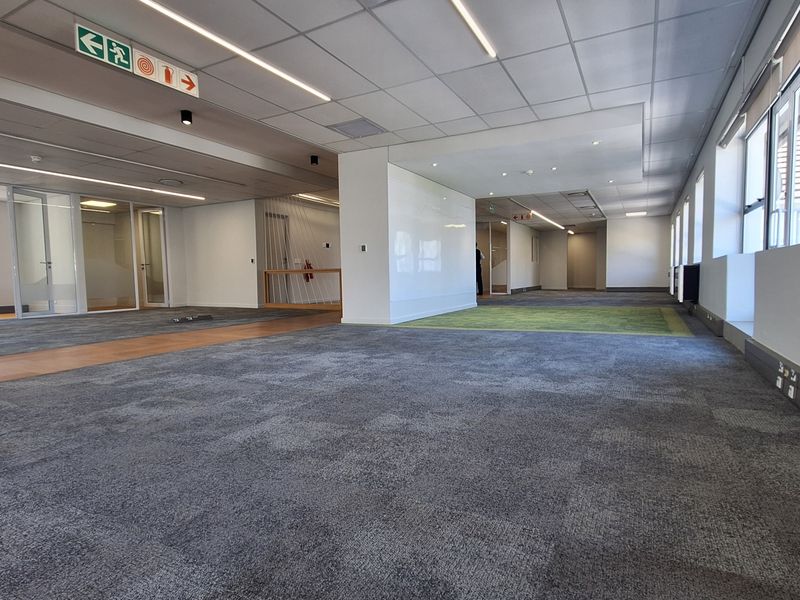 Spacious open-plan office area featuring modern carpet tiles, suspended ceilings with recessed lighting, and glass-partitioned meeting rooms, offering a clean and professional workspace.