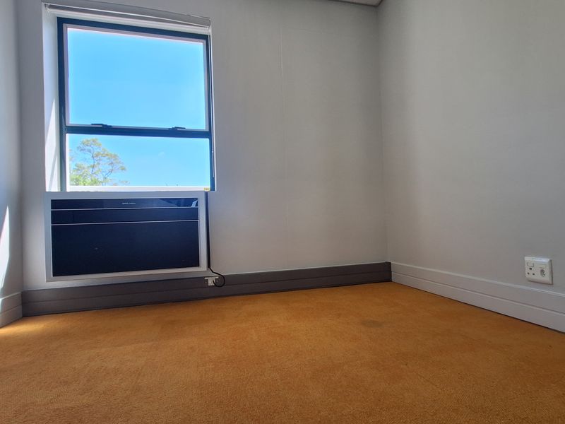 A vacant office space featuring neutral walls, a window with an integrated air conditioning unit, and carpeted flooring.