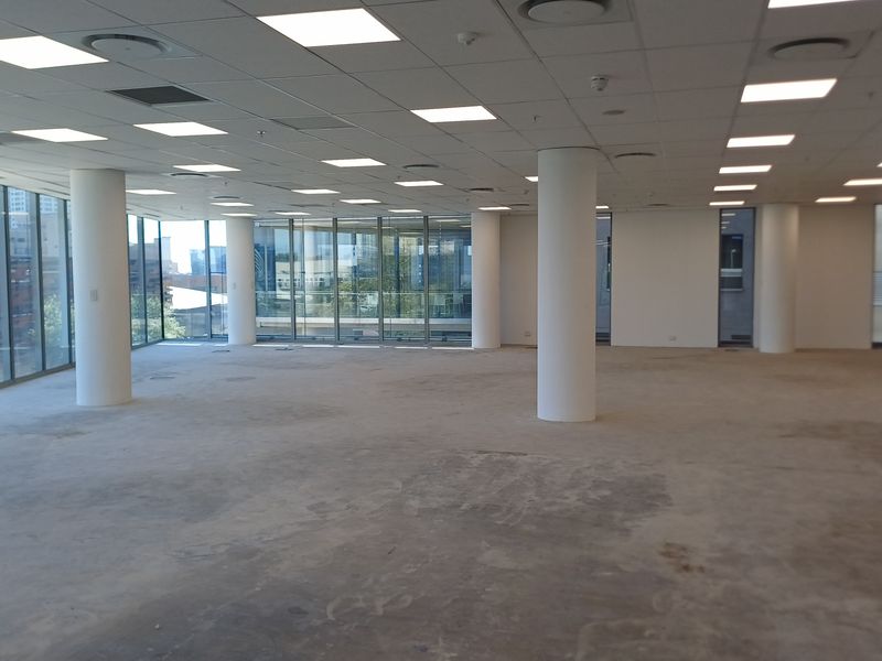 Spacious open-plan office area featuring floor-to-ceiling windows, recessed lighting, and a suspended ceiling, offering a bright and versatile workspace.