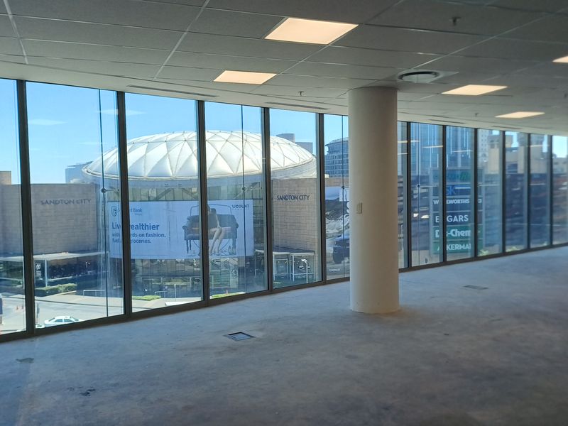 Spacious open-plan office area featuring floor-to-ceiling windows with views of Sandton City, suspended ceilings, and recessed lighting.