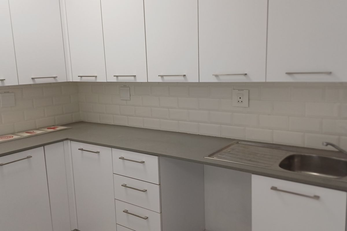 A clean, modern kitchen area featuring white cabinetry, a grey countertop, a stainless steel sink, and a classic subway tile backsplash.