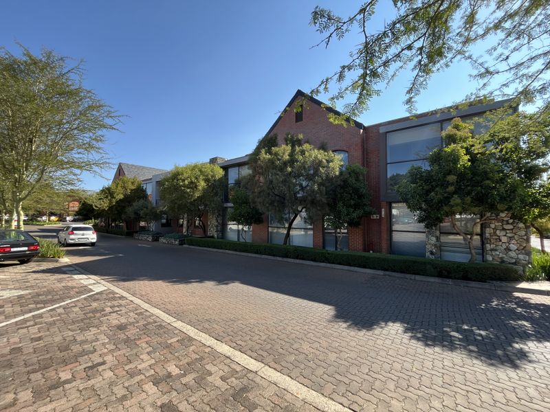 A well-maintained office building exterior featuring a combination of brick and stone cladding with large windows, set along a paved driveway.
