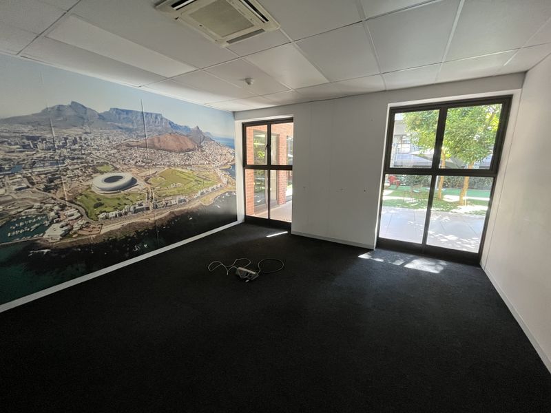 A bright, empty office space featuring a suspended ceiling, recessed air conditioning, and large windows overlooking the exterior.