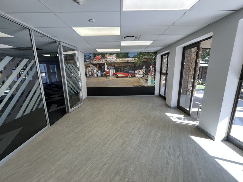 A bright, empty office space featuring modern glass partitions, wood-look flooring, and a decorative wall mural, suitable for a professional workspace.