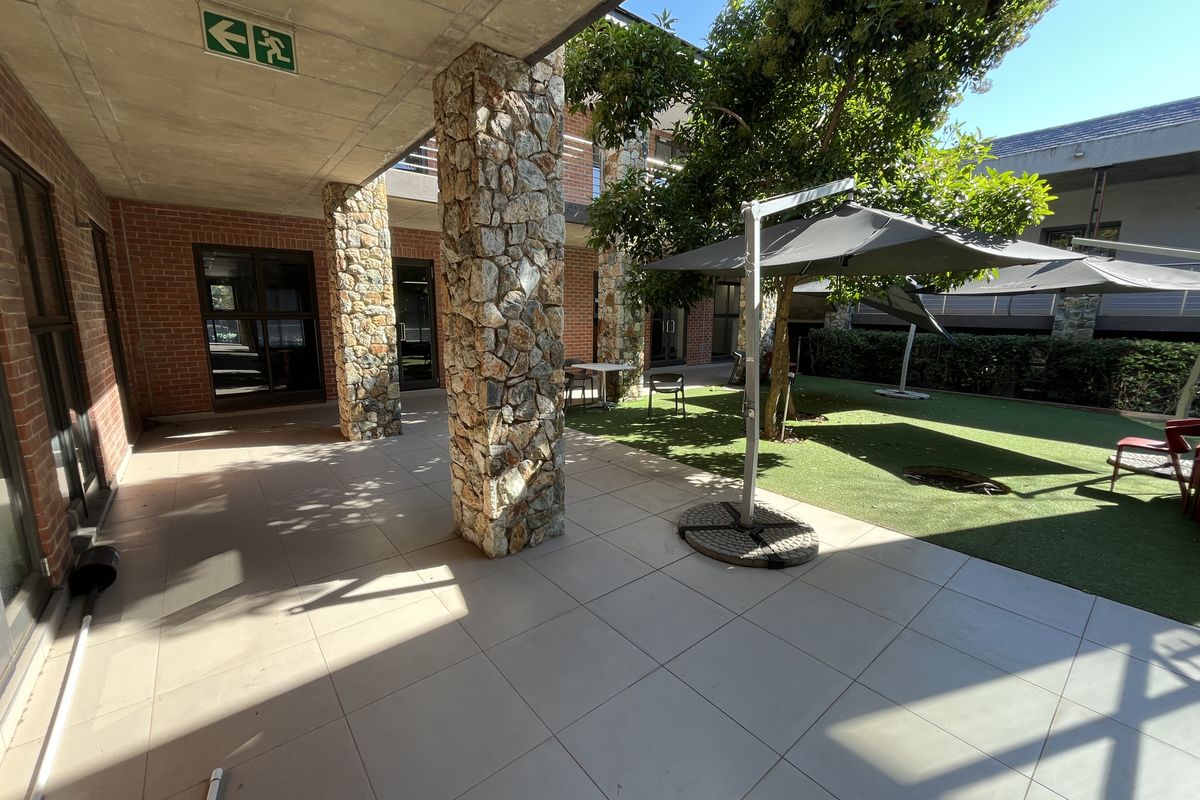 A covered outdoor patio area featuring stone-clad columns, exposed concrete ceilings, and tiled flooring, adjacent to a landscaped garden space.